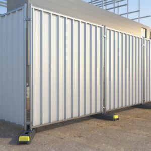 The image shows a series of vertical hoarding panels with a corrugated metal surface, set up around a construction site.